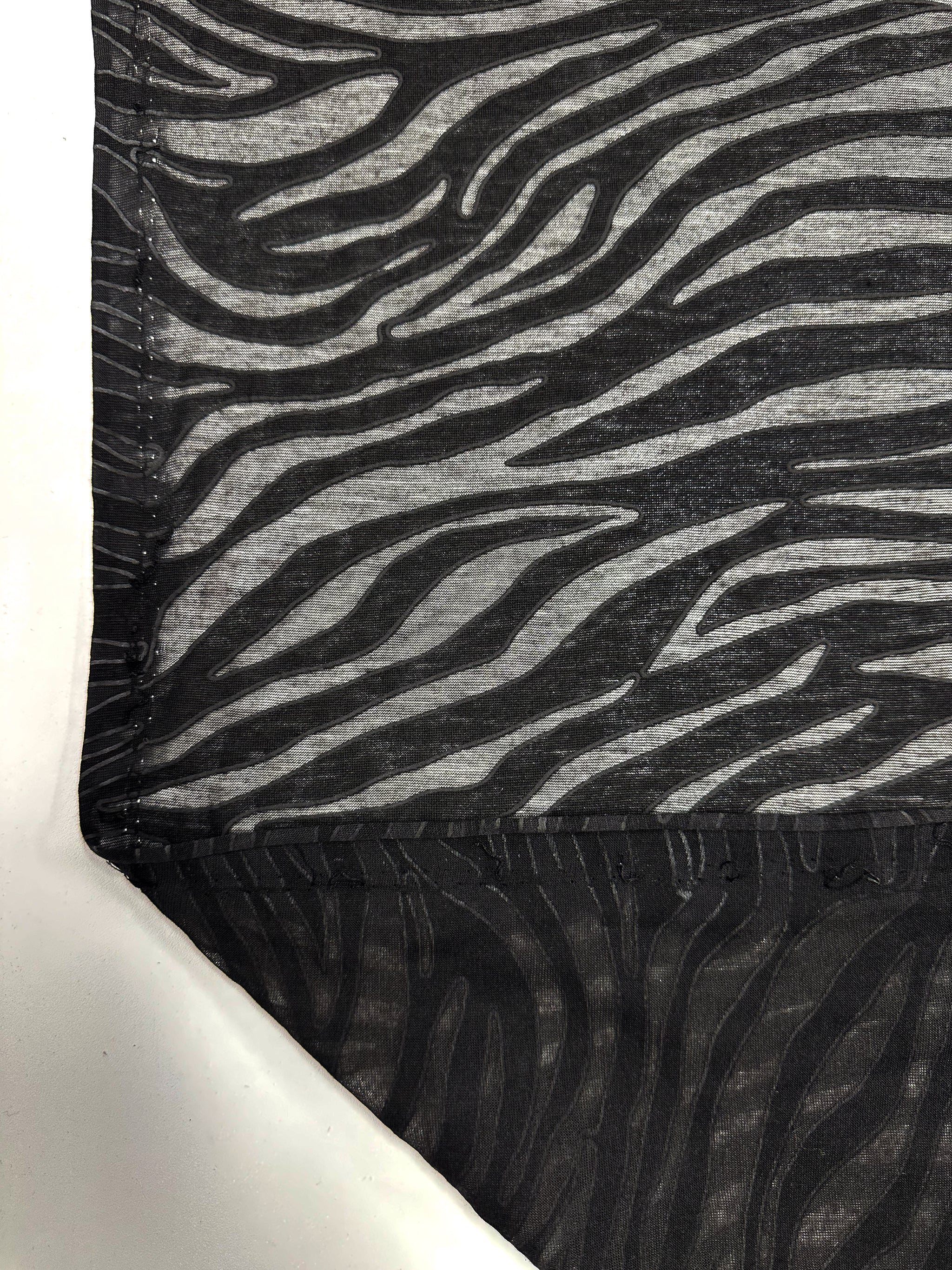 Close-up of Super Cheap Fabrics' Burnout Jersey - Zebra (160cm) with a black and gray zebra stripe. The textile layers reveal sheer and opaque sections, with a folded lower left corner showcasing texture and design contrast.