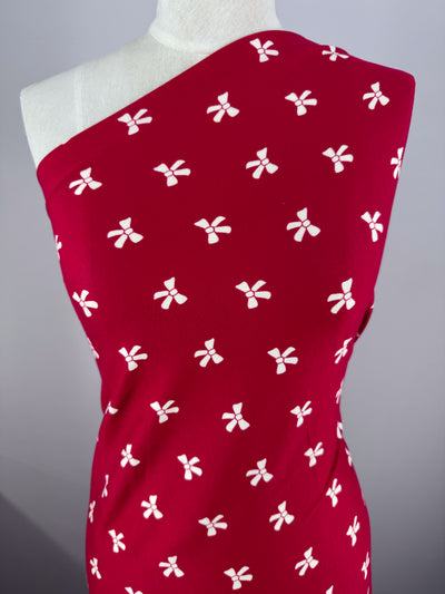 Displayed on a mannequin, the Urban Red dress by Super Cheap Fabrics is crafted from medium-weight Printed Cotton Lycra with a white floral pattern. It boasts a chic one-shoulder design against a plain gray background.
