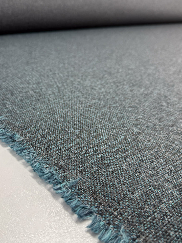 Close-up of Super Cheap Fabrics' Upholstery - Soho Topaz (150cm) in blue-gray, medium weight, with frayed edges on a white surface. The wool-look texture and threads are clearly visible.
