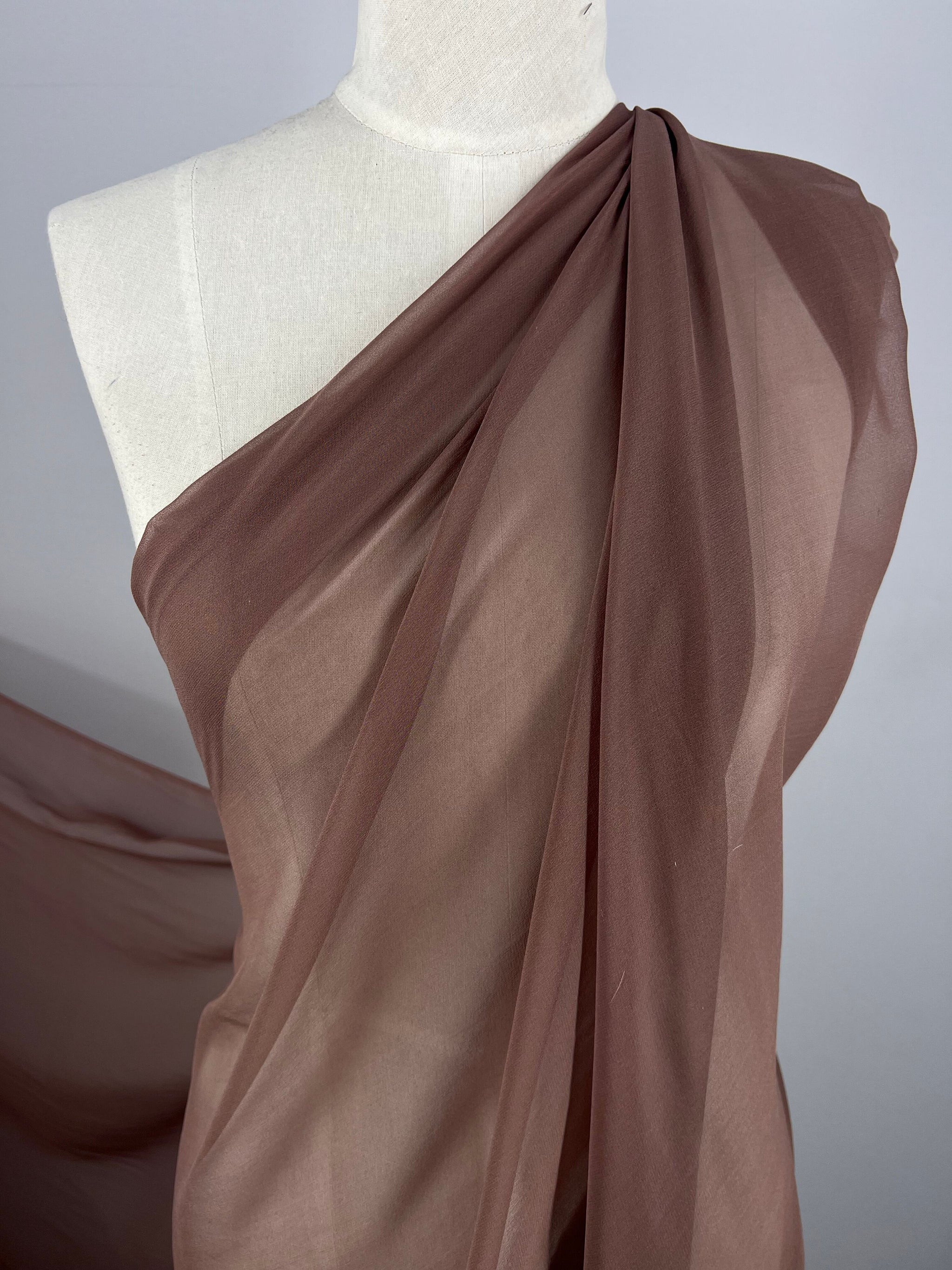 A dress form draped with Super Cheap Fabrics' Silk Georgette - Shroon - 135cm, wrapping gracefully over one shoulder and cascading downward. Set against a plain white background, this delicate and translucent fabric draws all the attention, making it an ideal choice for spring and summer outfits.