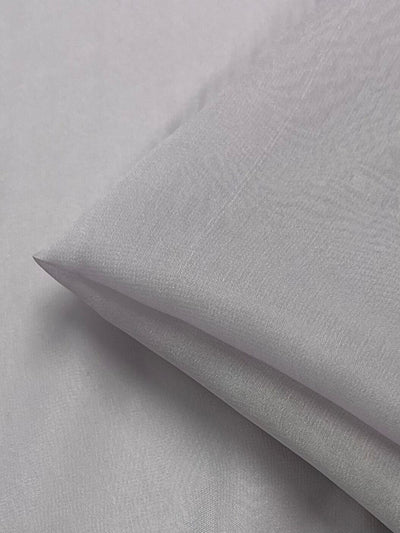 A close-up view of a neatly folded piece of light grey fabric reveals a smooth and slightly shiny texture. The Silk Georgette - Orkid - 135cm by Super Cheap Fabrics appears soft and lightweight, making it perfect for summer outfits.