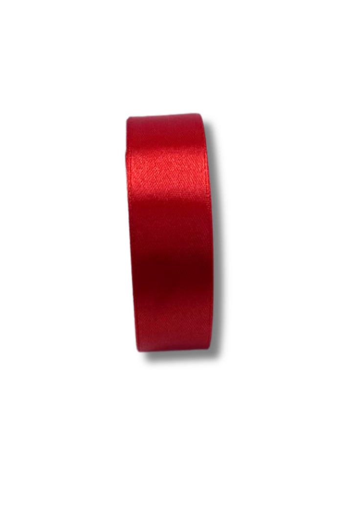 A roll of Super Cheap Fabrics’ Satin Ribbon - 16 Colours - 25mm, in shiny red, stands upright against a white background, casting a soft shadow to the right.