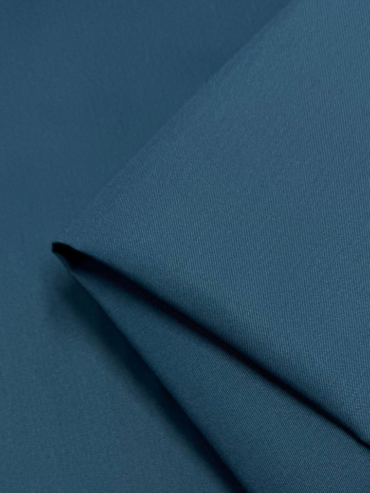 A close-up of the folded Gabardine fabric in teal from Super Cheap Fabrics showcases its smooth texture and rich color. This durable, wrinkle-resistant material subtly captures light on its tightly woven surface.