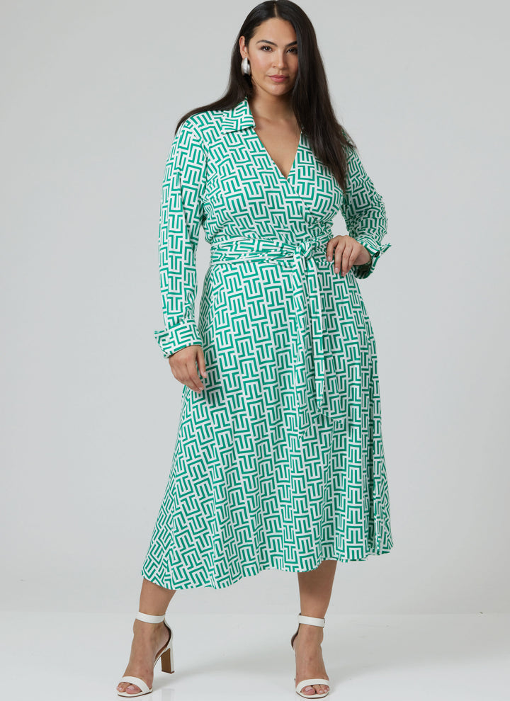 A woman wears the Pattern - Vogue - V2000 - Misses’ DVF Wrap Dress by Diane von Furstenberg from Super Cheap Fabrics in a green and white geometric print, with long sleeves and a tie belt, styled with white heeled sandals against a gray background.