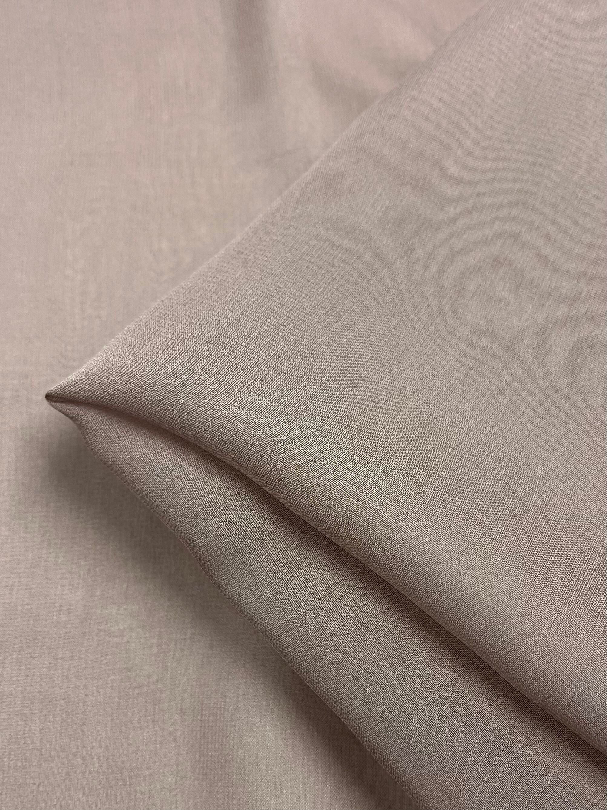 A close-up image of a piece of Silk Georgette - Quail from Super Cheap Fabrics, folded neatly. The light beige fabric exhibits a smooth and slightly reflective texture, indicating its fine, lightweight nature. The sharply defined edges of the fold suggest careful handling, making it ideal for crafting elegant summer outfits.