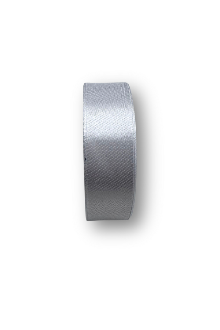 The Satin Ribbon - 16 Colours - 25mm by Super Cheap Fabrics is shown in a shiny, light gray roll standing upright against a plain white background.