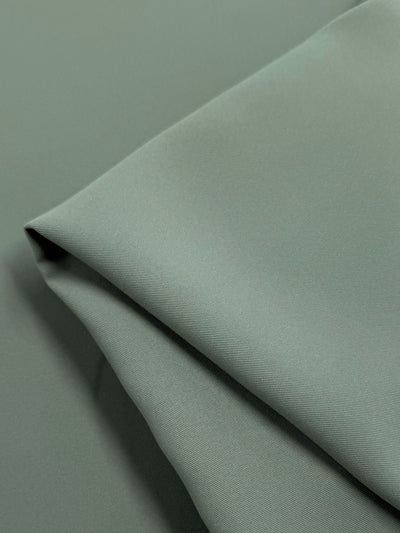 A detailed view of Super Cheap Fabrics' Microfibre Suiting in Dried Sage shows the medium-weight, light green fabric's subtly textured surface. The 150cm polyester appears soft and tidy, with clean lines and gentle shadows highlighting its elegant folds.