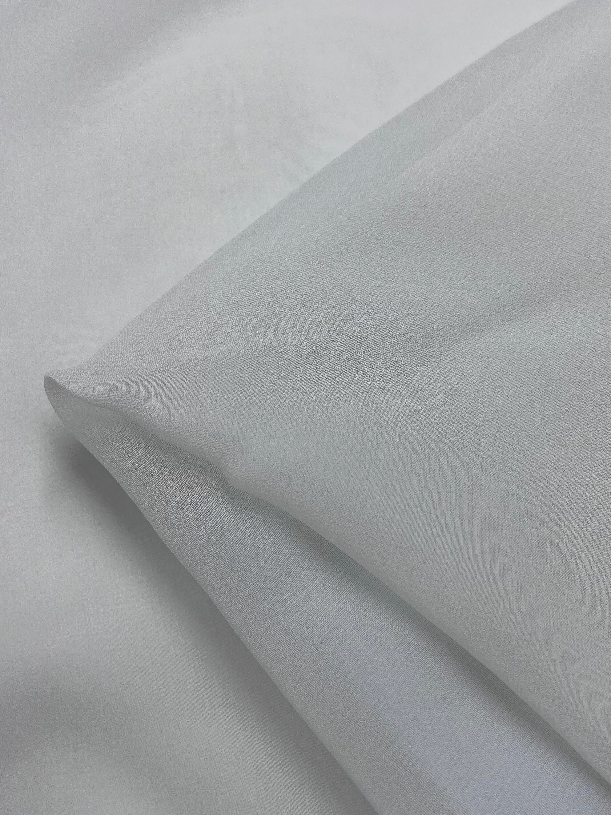 The Pure Silk Georgette in Silver Blue from Super Cheap Fabrics showcases a delicate texture and fine weave, ideal for spring and summer outfits. Its lightweight nature is evident with a slight fold at one corner. Width: 135cm.