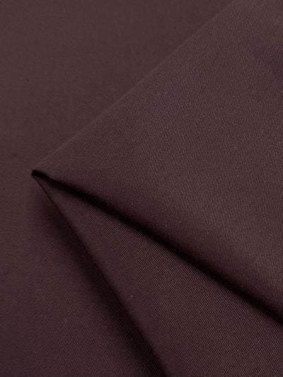 Close-up of Bitter Chocolate gabardine fabric by Super Cheap Fabrics, showcasing its texture and fine lines. The smooth, wrinkle-resistant surface with subtle shadows accentuates the diagonal fold. Width: 150cm.