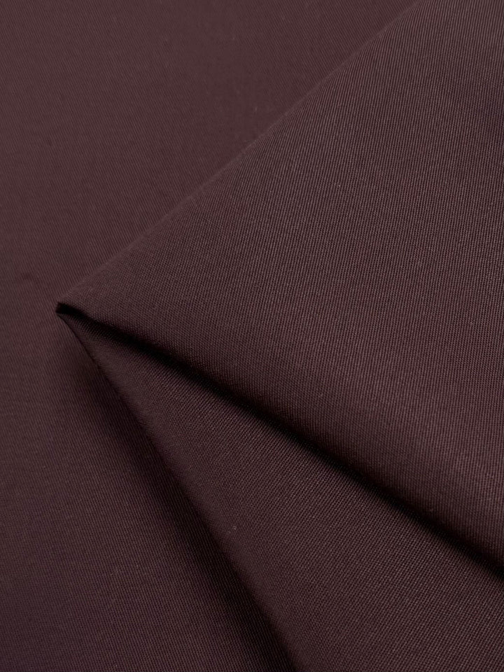 Close-up of Bitter Chocolate gabardine fabric by Super Cheap Fabrics, showcasing its texture and fine lines. The smooth, wrinkle-resistant surface with subtle shadows accentuates the diagonal fold. Width: 150cm.