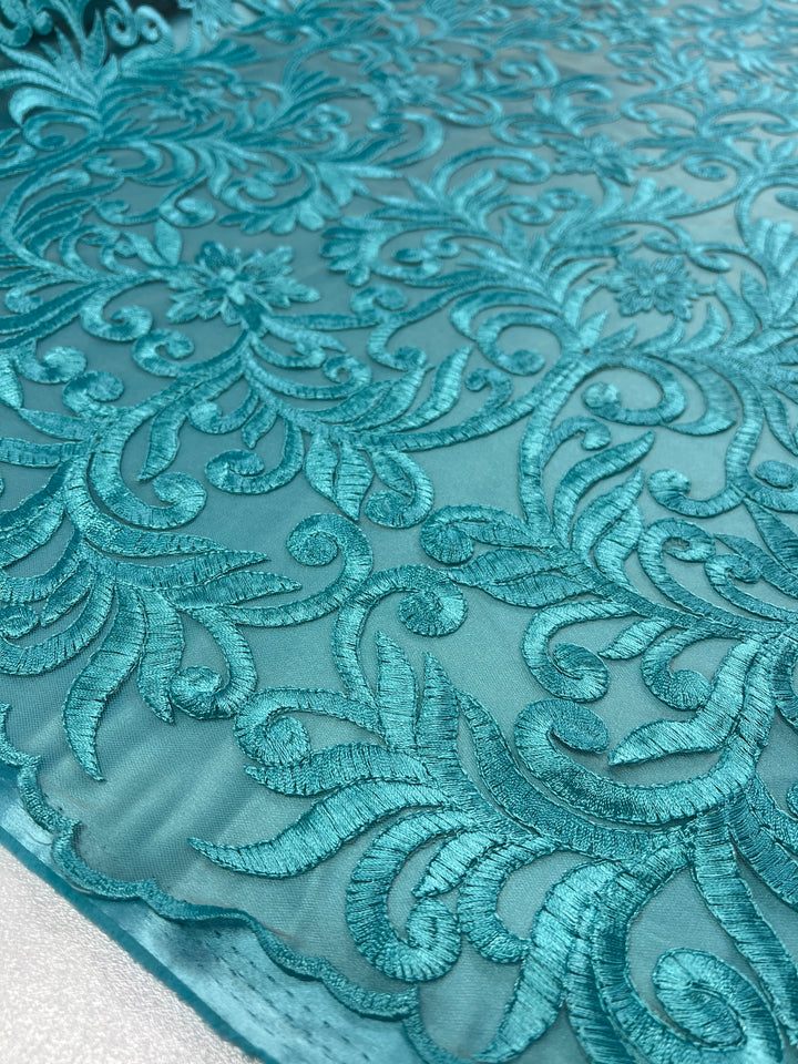 Close-up of a vibrant teal lace fabric with intricate floral embroidery. The Evening Lace - Aqua Galadriel - 125cm by Super Cheap Fabrics pattern features swirling leaves and flowers, showcasing fine detailing and a delicate texture. The material appears sheer and elegant, suitable for high-end fashion or decorative purposes.