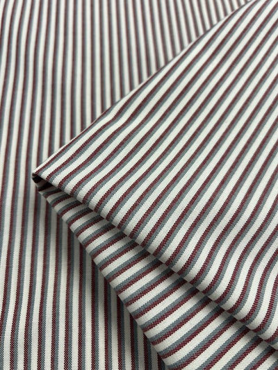 Close-up of Shirting - Hearted - 148cm by Super Cheap Fabrics, featuring lightweight polyester viscose with thin vertical maroon and white stripes, neatly folded to highlight the detailed weave and pattern.
