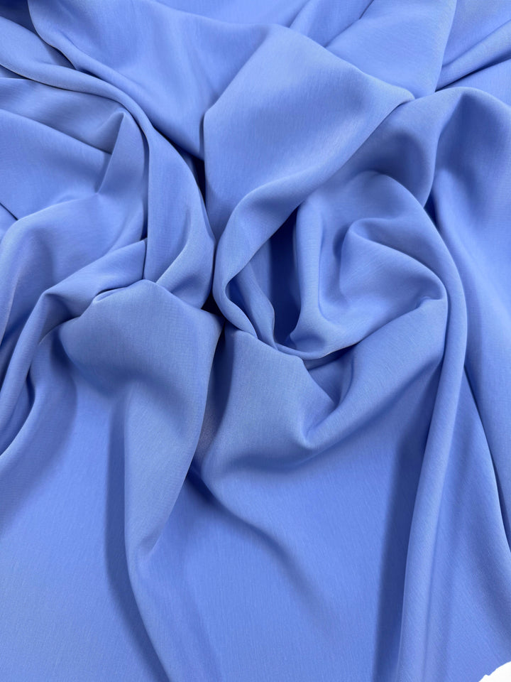 The Super Cheap Fabrics Microfibre Suiting in Azurine, measuring 150cm, drapes in soft folds with its silky, medium weight. Its light blue polyester surface forms flowing shadows and highlights, enhancing its smooth texture.