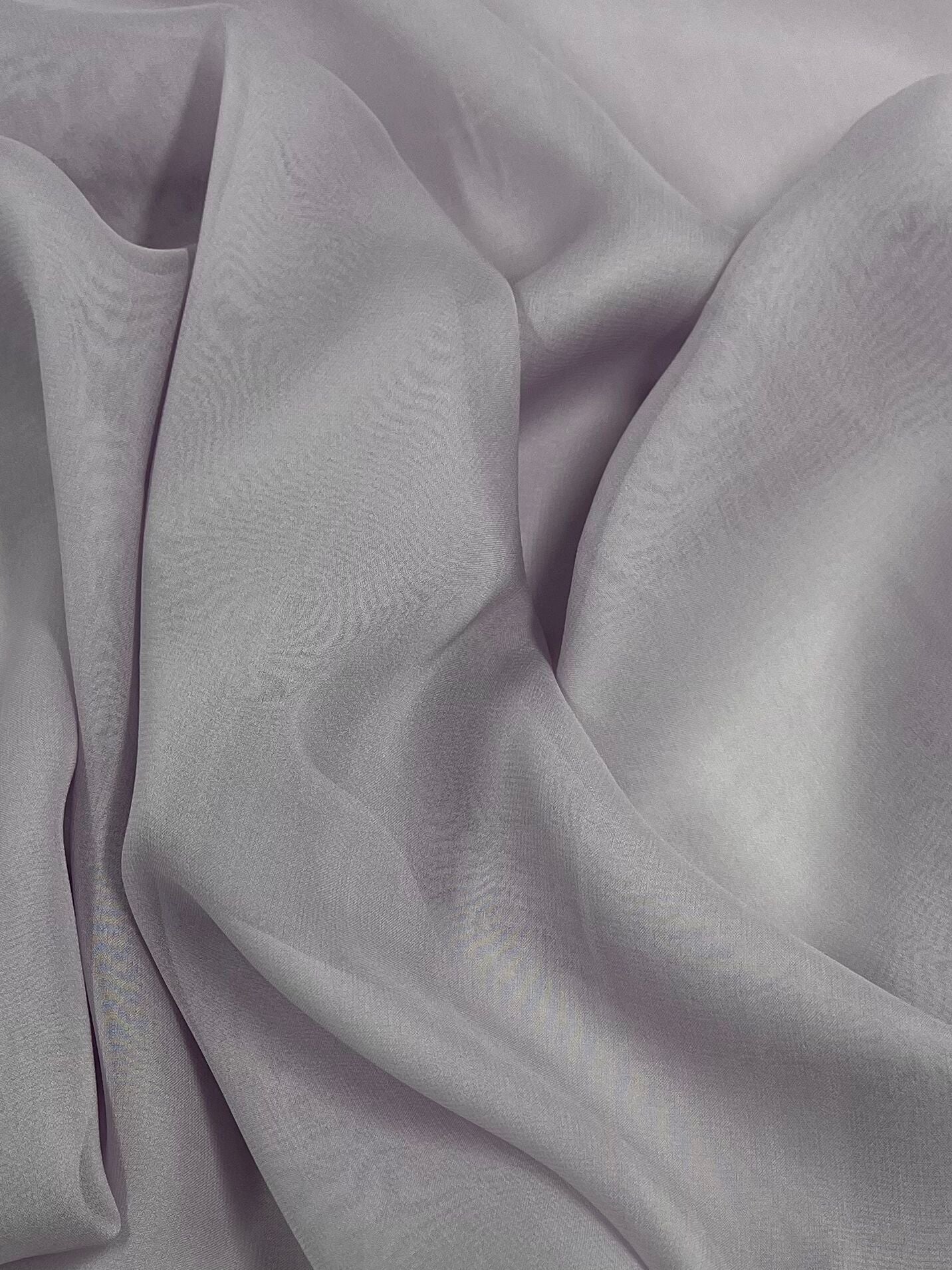 A close-up image features the luxurious texture of Super Cheap Fabrics' Silk Georgette - Orkid - 135cm in a soft, light grey hue. The gentle folds and creases highlight the smooth, silky surface that reflects light subtly, giving it a delicate sheen. The elegant draping creates a flowing pattern, making it an ideal choice for summer outfits.