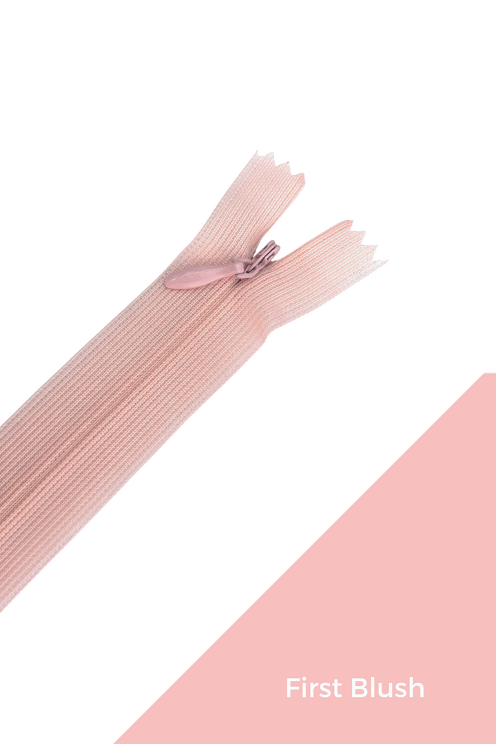 A light pink Super Cheap Fabrics Invisible Zip - 30cm - Pinks & Reds, made from 100% polyester, rests on a white and pale pink background with "First Blush" in the bottom right corner.