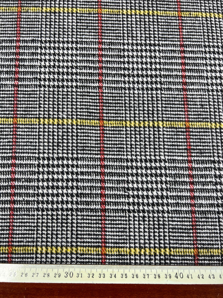 Super Cheap Fabrics' Wool Flannel - Redellow Plaid is a premium wool fabric with a black and white houndstooth pattern, overlaid with thin red and yellow grid lines. Displayed on wood, the fabric includes a measuring tape showing an approximate width of 42 cm.