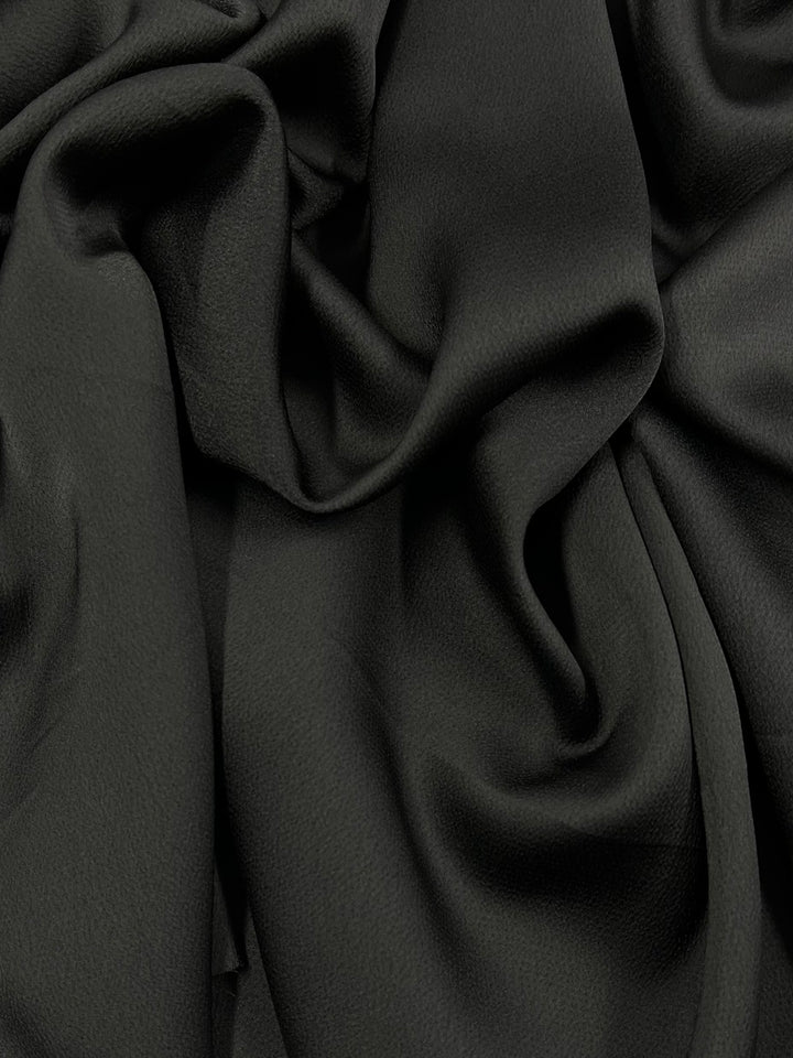A close-up image of black, medium weight fabric with soft folds and drapes. The Crepe De Chine - Black - 150cm by Super Cheap Fabrics appears to have a slight sheen and a rich, luxurious texture.