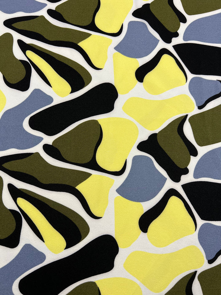 The Super Cheap Fabrics' Printed Crepe - Camo Special showcases irregular black, yellow, olive green, and gray shapes on white. Made from lightweight polyester, this modern camouflage design is perfect for versatile use. Width: 150cm.