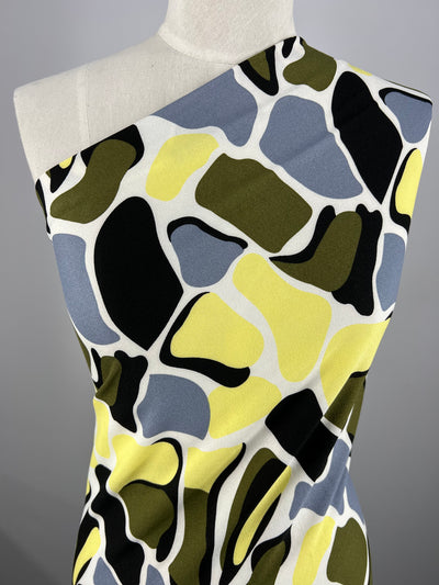The Printed Crepe - Camo Special - 150cm by Super Cheap Fabrics showcases a bold abstract pattern crafted from lightweight polyester with irregular shapes in black, olive green, yellow, and gray for a dynamic and modern look.