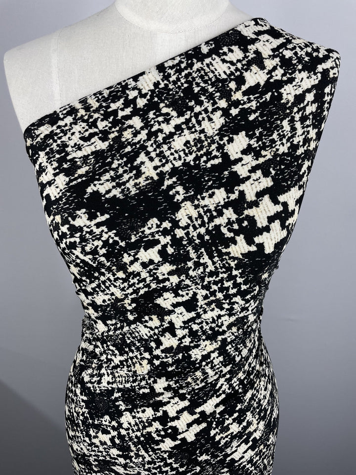 A close-up of a mannequin in a one-shoulder dress made from Super Cheap Fabrics' Printed Lycra - Blotched (150cm), featuring a black and white abstract pattern on two-way stretch polyester spandex, set against a plain background.