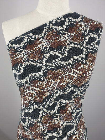 A mannequin wears a one-shoulder garment in brown, black, and white snake print using Super Cheap Fabrics' Printed Lycra - Venom (150cm), a two-way stretch Polyester Spandex that fits snugly and drapes smoothly over the torso.